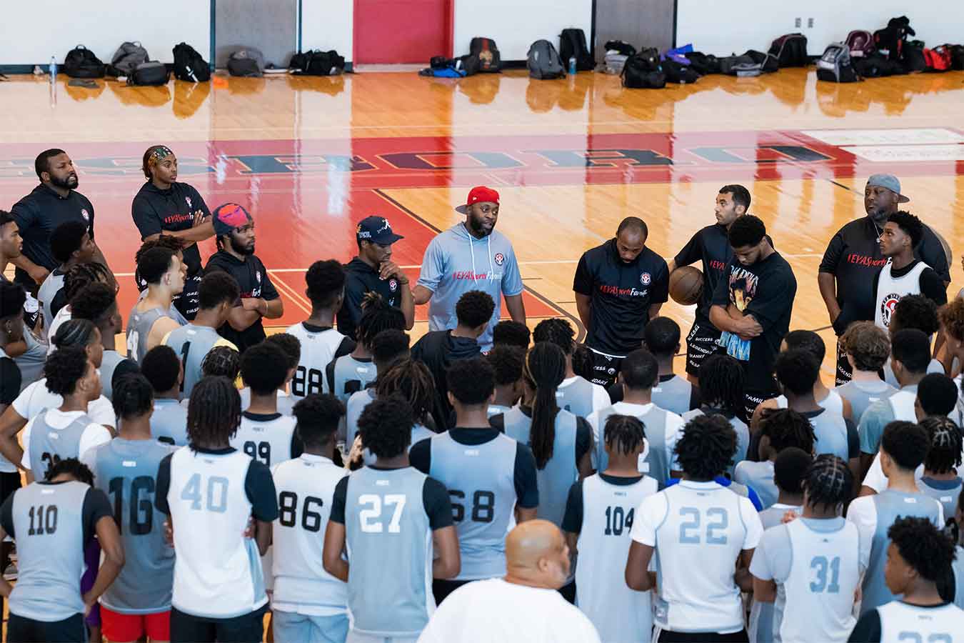 Braderious Martin (pictured center wearing a grey short-sleeve hoodie and red hat talks to basketball players.