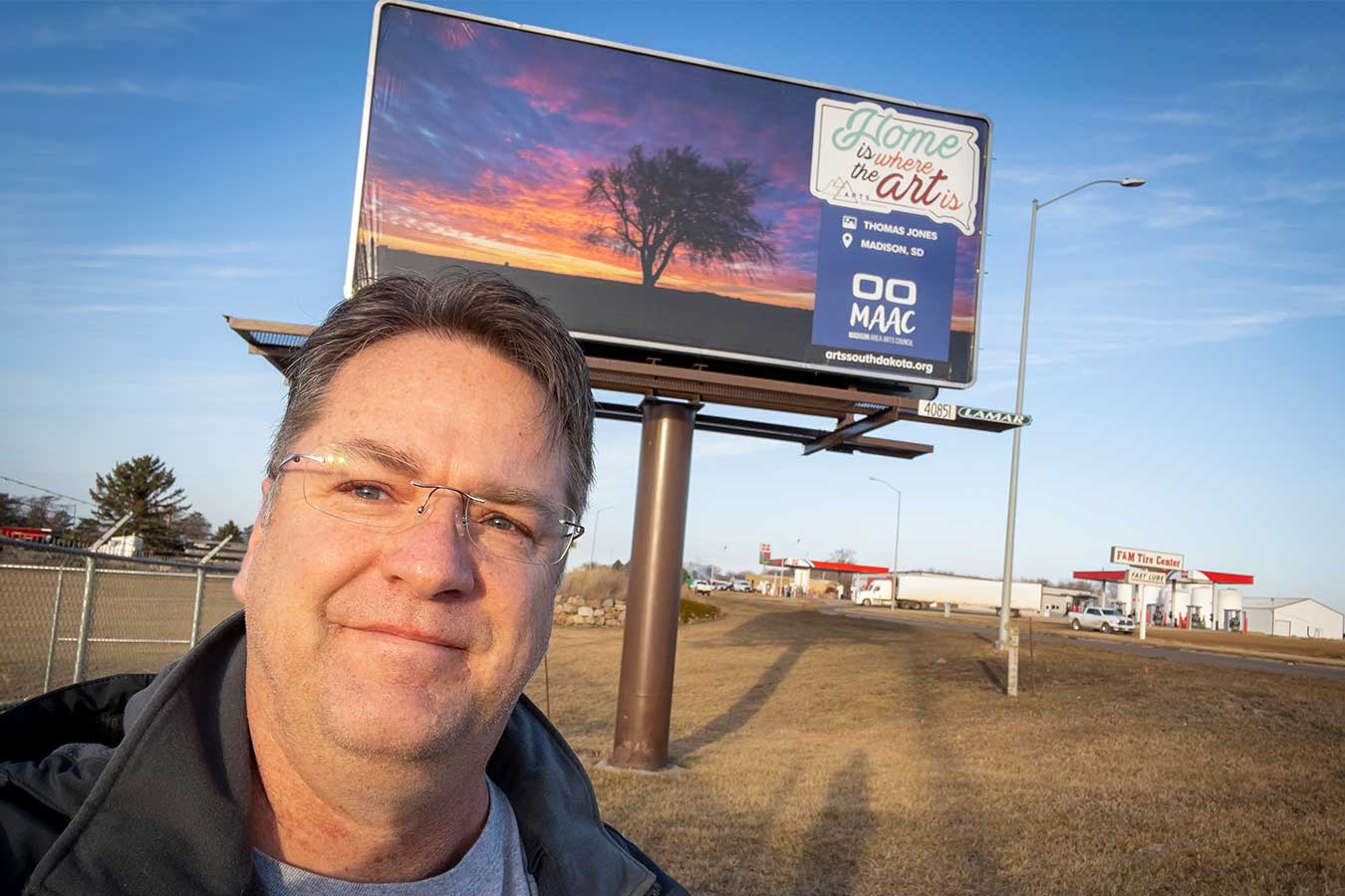 Tom Jones in front of the billboard featuring his photo of a lone tree at sunset near Madison.