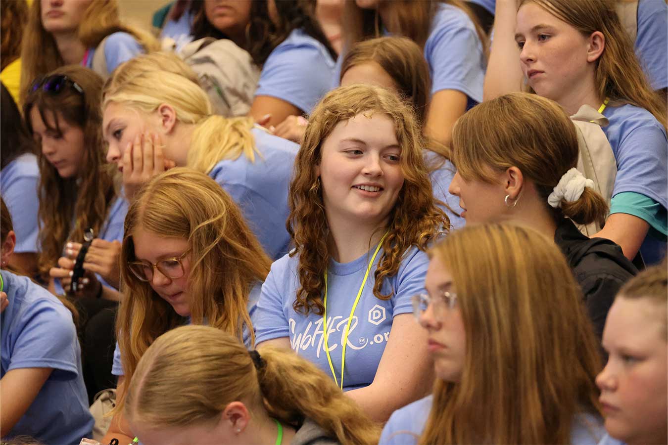 A girl attending CybHER Camp smiles while chatting with another student in a crowd.