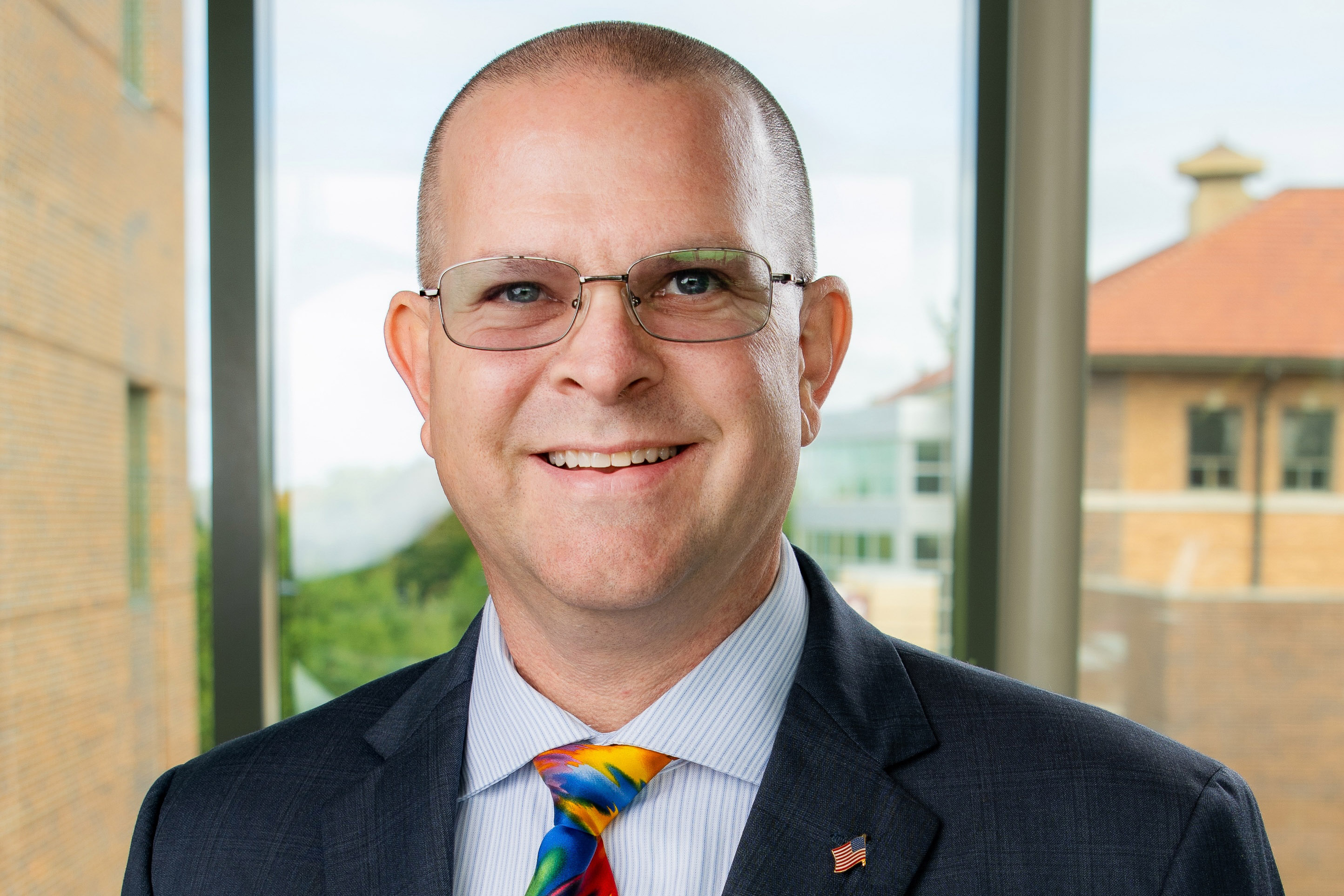 Darrel Sandall in blue suite with multi-colored tie in front of campus building backdrop